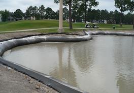 Lake shoreline restoration depicting dregesox repair. The shore is graded and a sediment filled tube is staked to the shore.